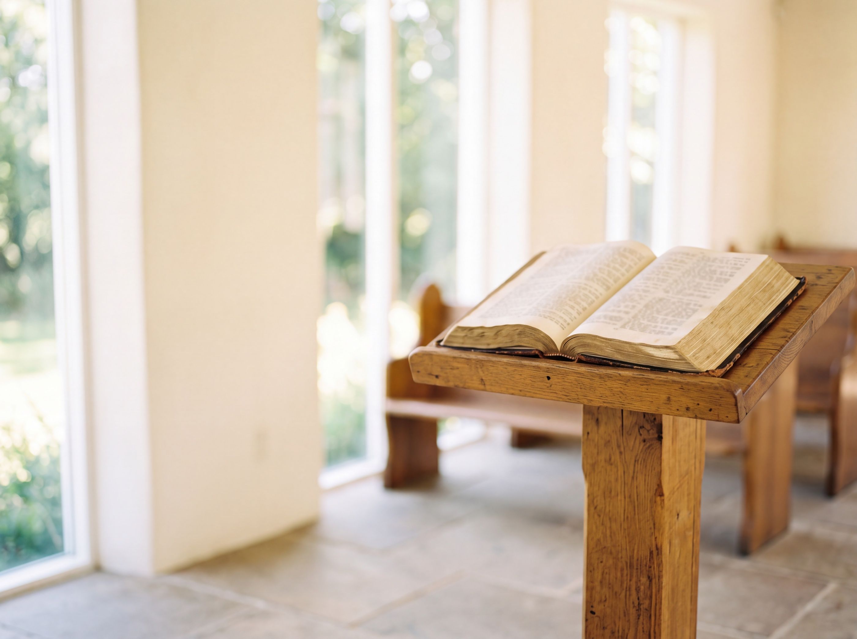 An open Bible on a wooden lectern in a bright, quiet chapel