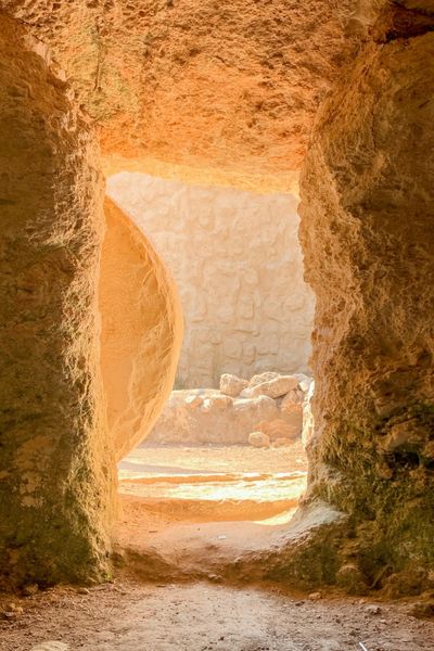 Morning light shining into an empty rock-cut tomb with the stone rolled away